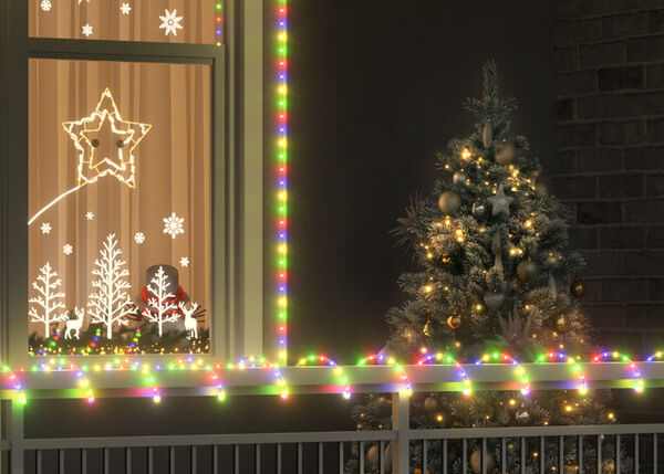 Scenă de Crăciun &icirc;n aer liber cu un brad decorat cu globuri aurii și lumini l&acirc;ngă o fereastră &icirc;ncadrată de luminițe multicolore. Fereastra are decorațiuni luminoase cu stele, fulgi de zăpadă și forme de copaci, iar pe fereastra alăturată este at&acirc;rnată o coroană cu fundă roșie.