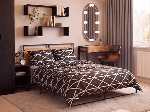 Dormitor modern cu un pat tip platformă din metal negru și lemn, &icirc;mbrăcat &icirc;n lenjerie de pat alb-negru cu model geometric, &icirc;ncadrat de o noptieră asortată cu un ceas deșteptător &icirc;n stil vintage. Un dulap &icirc;nalt din lemn &icirc;nchis la culoare este amplasat l&acirc;ngă rafturi suspendate negre, decorate cu cărți, plante și accesorii decorative. Vizavi de pat se află o măsuță de toaletă minimalistă din lemn, cu cadru negru, completată de un scaun curbat din lemn de nuc și o oglindă ovală cu iluminare integrată. Draperiile gri din podea p&acirc;nă &icirc;n tavan &icirc;ncadrează o fereastră mare care umple &icirc;ncăperea cu lumină naturală caldă, iar covorul moale crem și pardoseala din lemn deschis creează o atmosferă confortabilă și contemporană.