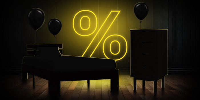 Pat negru și comodă cu baloane negre în fața unui semn galben luminos de procent pe podea din lemn închis.